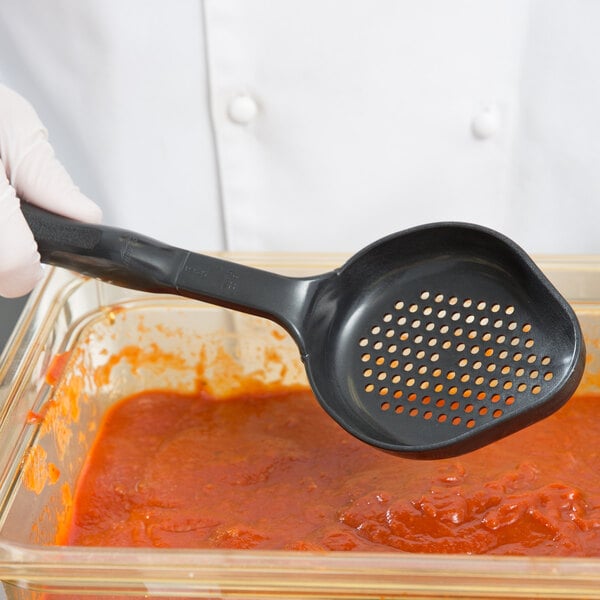 A person using a Vollrath High Heat Perforated Oval Nylon Spoodle to serve red sauce.
