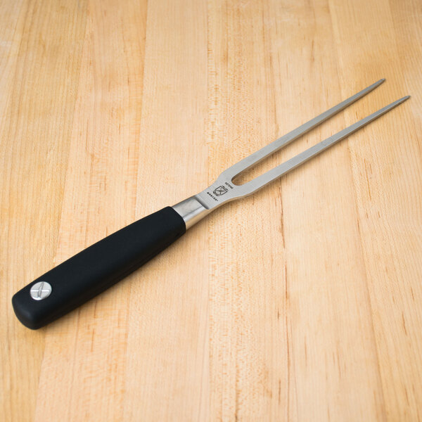 A Mercer Culinary Genesis forged carving fork with a black handle and full tang blade on a wooden table.