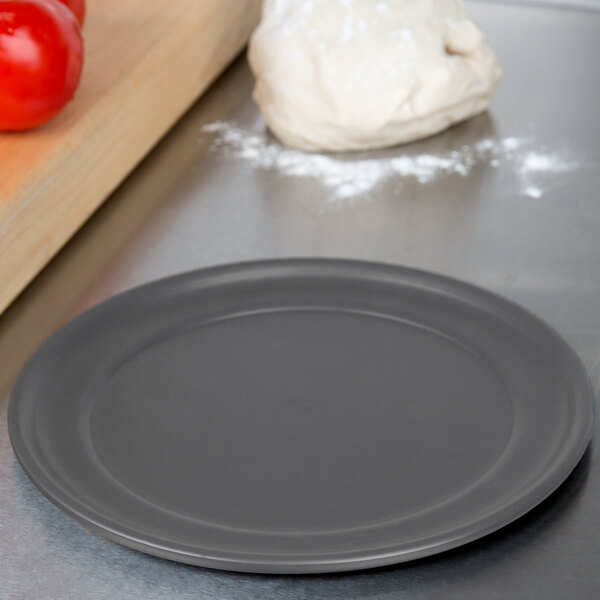 A ball of pizza dough on an American Metalcraft Hard Coat Anodized Aluminum Pizza Pan on a counter.