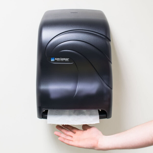 A hand using a San Jamar black paper towel dispenser.