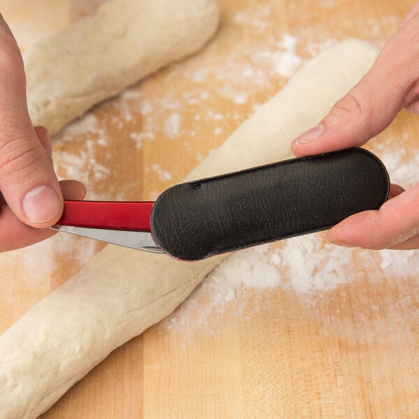 A person using a Victorinox aluminum folding bread lame to cut dough.