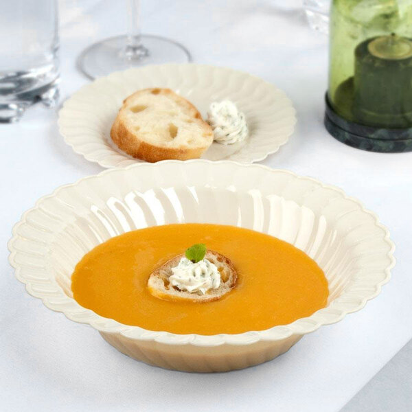 A Fineline Flairware ivory plastic bowl filled with soup and a piece of bread on a table.