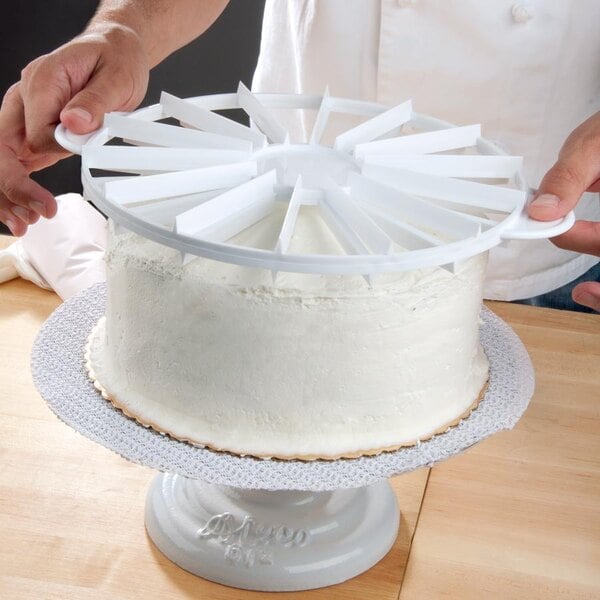 A hand uses an Ateco Double-Sided Cake Marker to cut a white cake on a stand.
