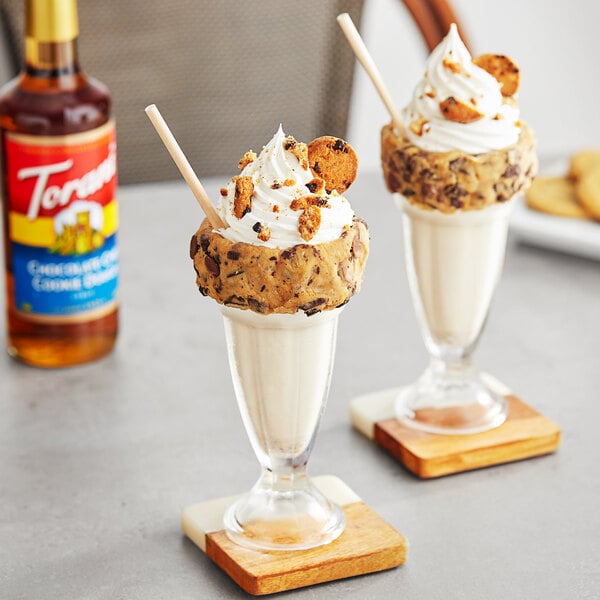 Two glasses of ice cream with cookies on top and a bottle of Torani Chocolate Chip Cookie Dough flavoring syrup.