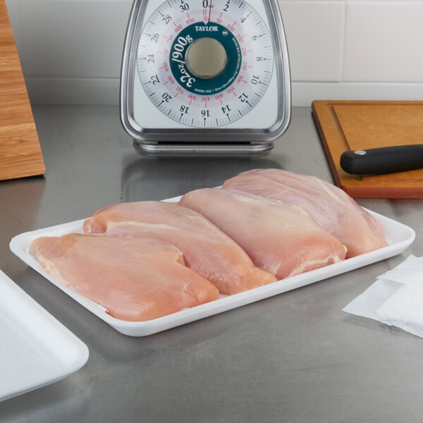 A white foam meat tray with raw chicken meat on a counter.