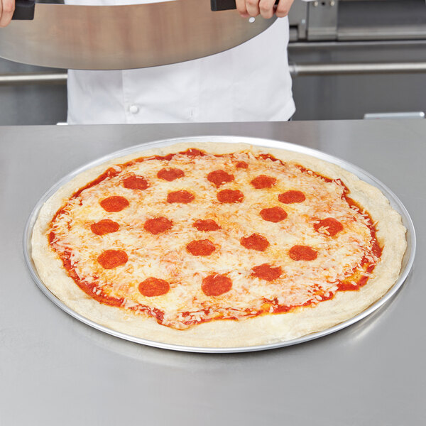 A person holding a pepperoni pizza on an American Metalcraft aluminum wide rim pizza pan.