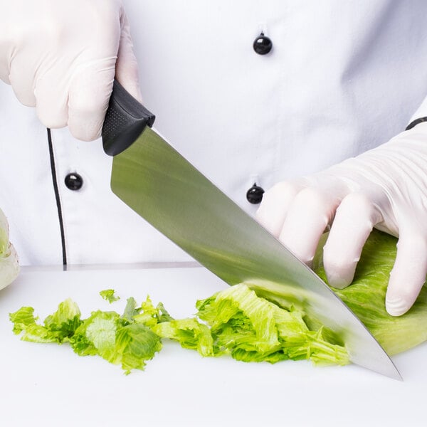A gloved hand uses a Mercer Culinary Millennia chef knife to cut lettuce.
