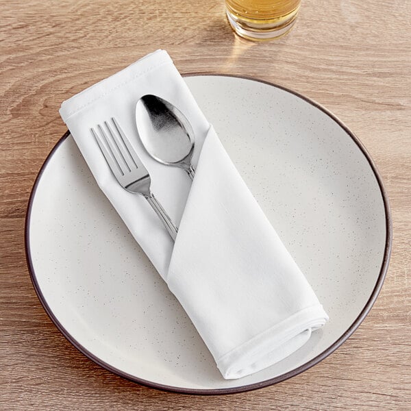 A white plate with a fork and spoon on a white Intedge cloth napkin.