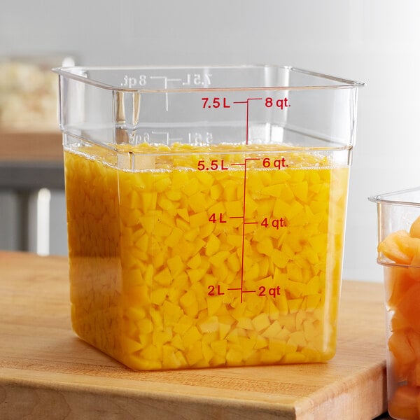A Cambro CamSquare food storage container filled with yellow food next to a measuring cup.