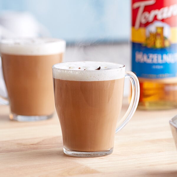 A glass mug of coffee with Torani hazelnut flavoring syrup and foam on top.