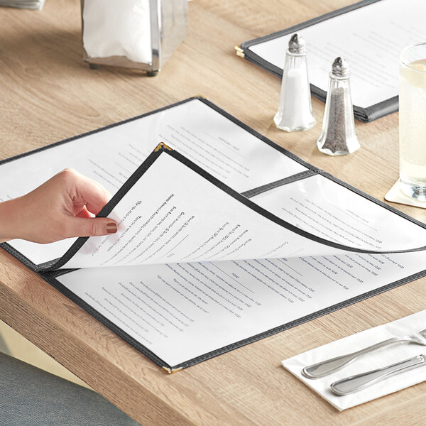 A hand opening a black 6-view three pocket menu cover on a table in a farm-to-table restaurant.