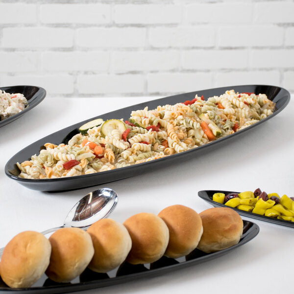 A black Siciliano oval platter with bread, rolls, and pasta on a table.