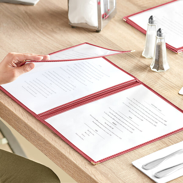 A woman's hand holding a burgundy 6-view trifold menu cover on a table.