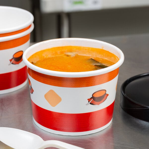 A white double poly-coated paper soup cup filled with soup with a black paper lid on a table.
