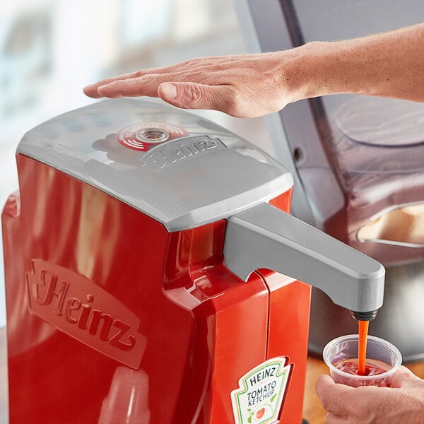A person using a Heinz automatic touchless pump lid to pour a drink into a cup.