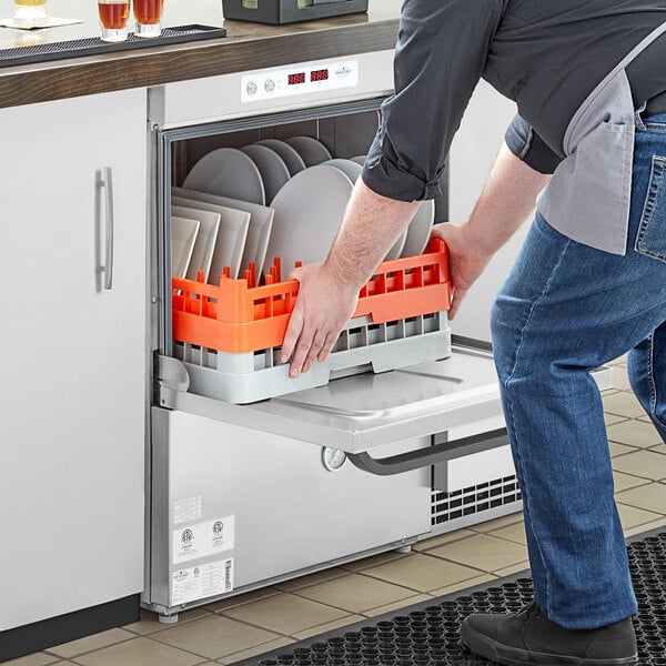 A man putting plates in a Main Street Equipment undercounter dishwasher on a counter in a professional kitchen.