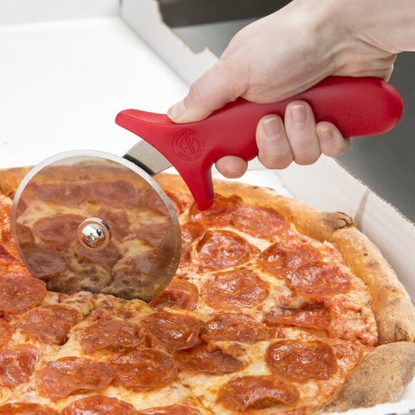 A person using an American Metalcraft stainless steel pizza cutter with a red handle to cut a pizza.