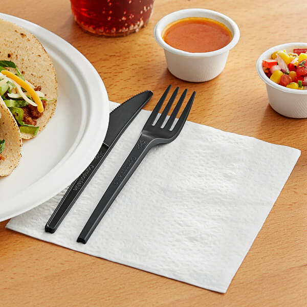 A plate of tacos with a fork and knife on a bamboo luncheon napkin.