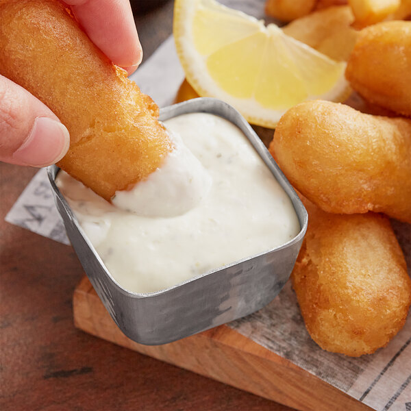 A hand dipping fried fish into a container of Admiration Tartar Sauce.