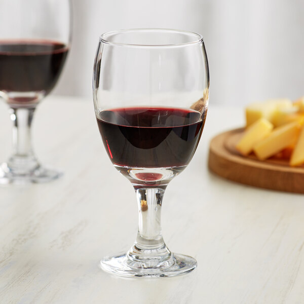 A close up of two Acopa glass goblets filled with red wine next to a plate of cheese.