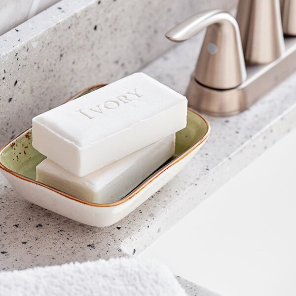 A white bar of Ivory Aloe Scent soap in a green soap dish on a counter.