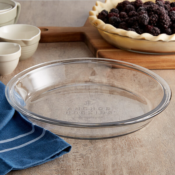 An Anchor Hocking glass pie dish with blackberries on a table with a blue towel.