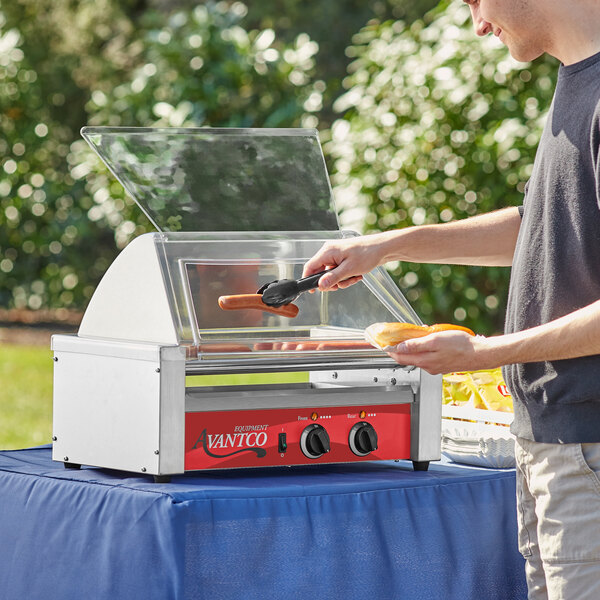 A man cooking hotdogs on an Avantco hot dog roller grill on a table outdoors.