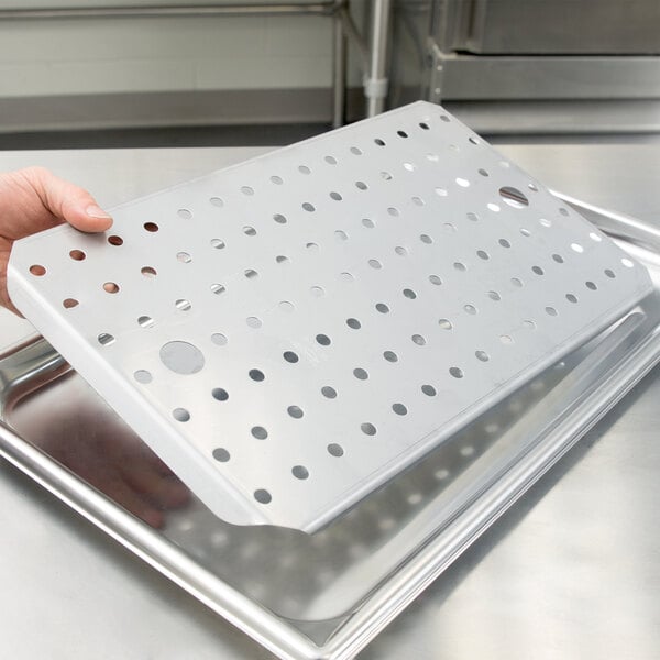 A hand holding a Vollrath stainless steel false bottom with holes in it.