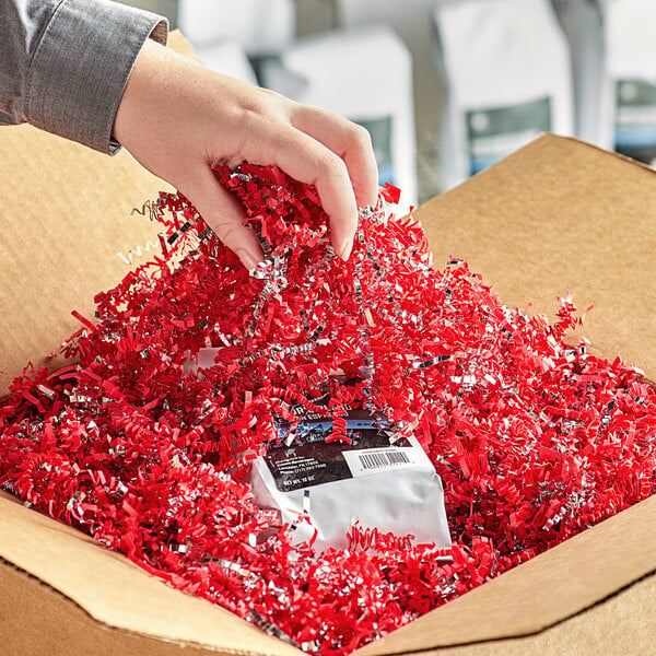 A hand putting Spring-Fill silver and red crinkle cut paper shred into a box.