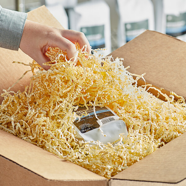 A hand holding a package in a box with Spring-Fill French Vanilla crinkle cut paper shred.