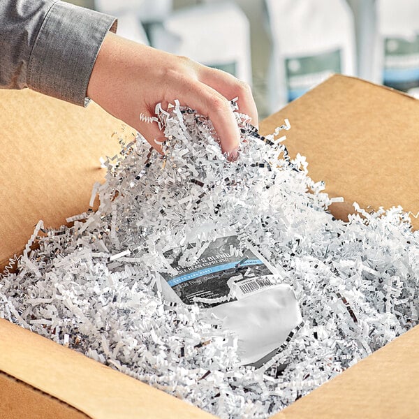 A person's hand holding a box of Spring-Fill silver and white shredded paper.