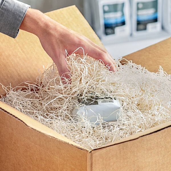 A hand reaching into a box filled with Spring-Fill ivory shredded paper.