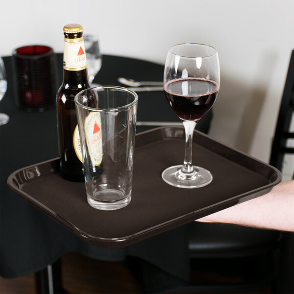 A person holding a Cambro Non-Skid Serving Tray with wine glasses and a bottle on it.