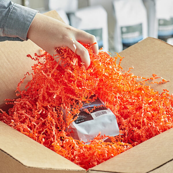 A hand holding a package of Spring-Fill orange shredded paper opening a box.
