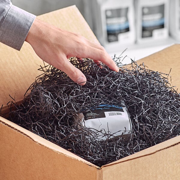 A hand holding a package in a box with Spring-Fill black shredded paper.