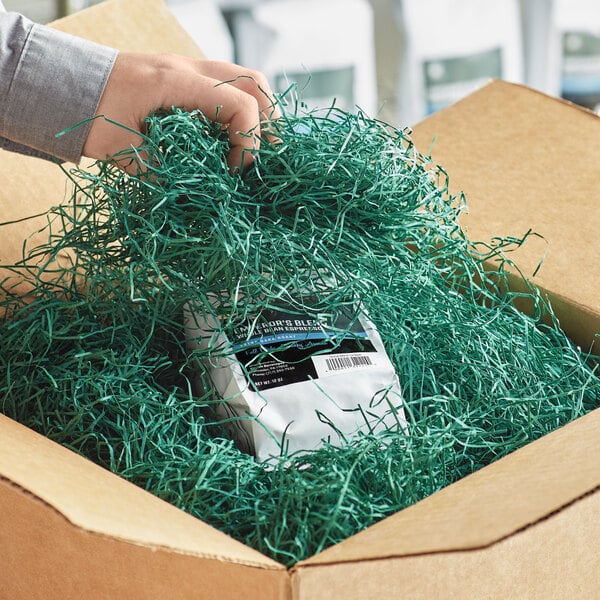 A person's hand holding a box filled with Spring-Fill Forest Green shredded paper.