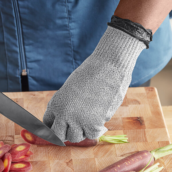A person wearing a Schraf gray cut-resistant glove cutting carrots on a counter.