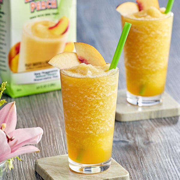 Two glasses of peach smoothie with straws and a peach slice, with a bag of peaches in the background.