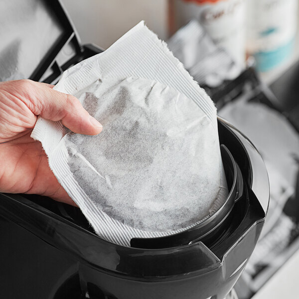 A hand using a white paper filter pack in a black Cuisinart coffee machine.