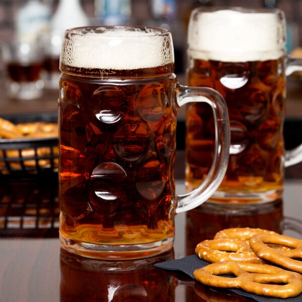 Two Stolzle glass mugs of Oktoberfest beer on a table with pretzels.