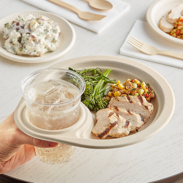 A hand holding a World Centric compostable fiber plate over a table of food.