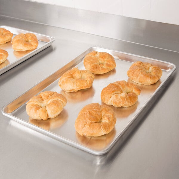 A Vollrath Wear-Ever bun pan filled with croissants on a stainless steel counter.