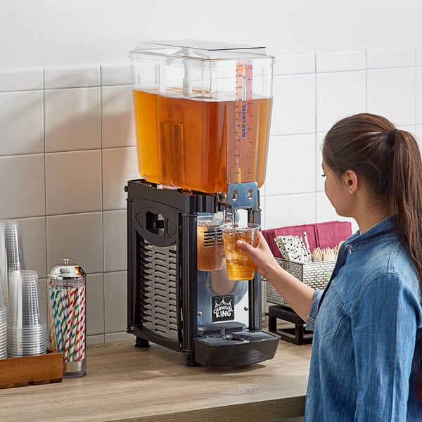 A woman pouring orange liquid into a Carnival King refrigerated beverage dispenser.