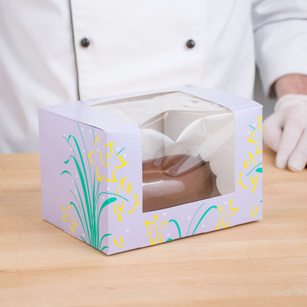 A person holding a white Easter egg candy box with a clear plastic window with chocolate eggs inside.