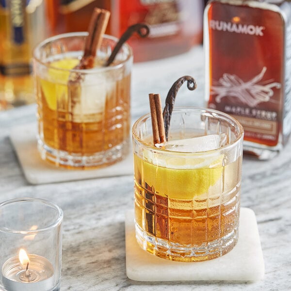 Two glasses of brown liquid with cinnamon sticks on a table.