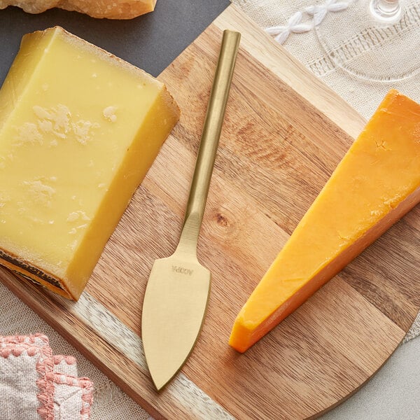 An Acopa gold stainless steel cheese knife cutting cheese on a wooden board.