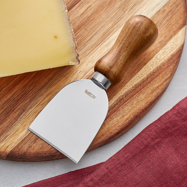 An Acopa stainless steel cheese knife with a dark wood handle on a wooden board.
