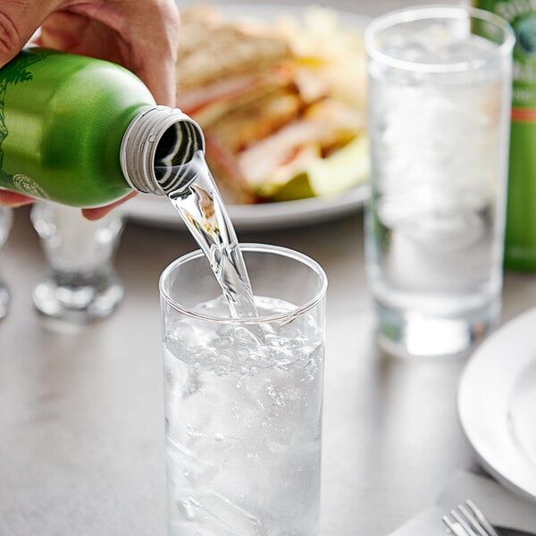 A person pouring Mountain Valley Spring Water from a green aluminum bottle into a glass.