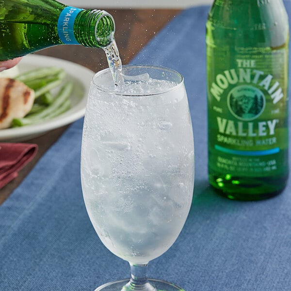 A person pouring Mountain Valley Sparkling Water from a green glass bottle into a small glass.