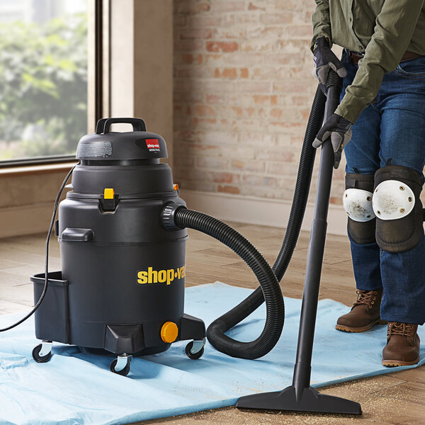 A man using a Shop-Vac wet/dry vacuum to clean a carpet in a room.